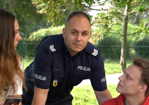 Policjant stoi przy ławce, na której siedzi dziewczyna i chłopak