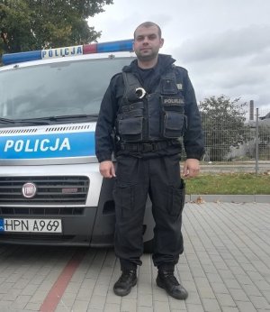 Policjant w mundurze na tle radiowozu.
