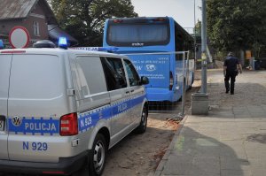 Policyjny radiowóz, w tle autobus i policjant.