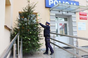 Policjantka drogówki stroi w odblaski choinkę przed budynkiem KPP Bytów.